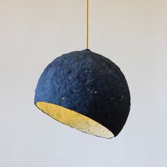 a blue and gold lamp hanging from a yellow cord on a white wall in a room