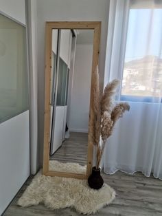 a tall mirror sitting on top of a wooden floor next to a white rug and window