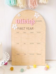 a wooden first year calendar with flowers and tassels hanging from the wall next to a cake