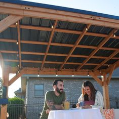 a man and woman sitting at a table under a pergolated roof with lights