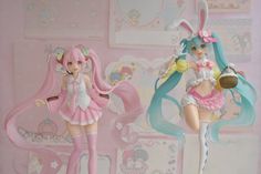 two figurines are posed in front of a wall with pink and blue decorations