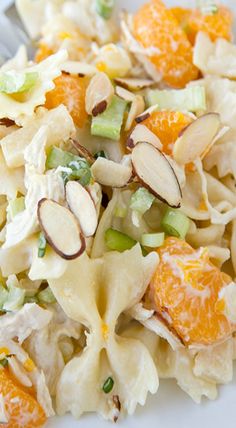 a white plate topped with pasta salad covered in nuts and oranges next to a fork