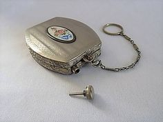 a small metal box with a key chain attached to it's side and a flowered design on the front