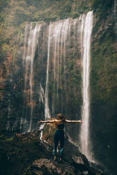 a woman standing in front of a waterfall with her arms spread out to the side