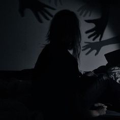 a person sitting on a bed in the dark with their shadow cast onto the wall