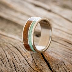 a wooden ring with green and white inlays sitting on top of a piece of wood