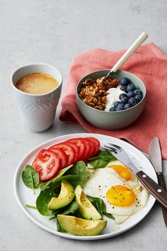 a white plate topped with an egg, tomato and avocado next to a cup of coffee