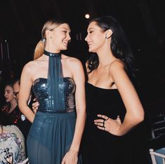 two beautiful women standing next to each other in front of a crowd at a party