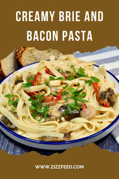 a white plate topped with pasta covered in sauce and vegetables next to bread on a table