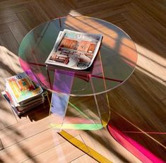 a glass table with magazines on it in the middle of a wooden floored room