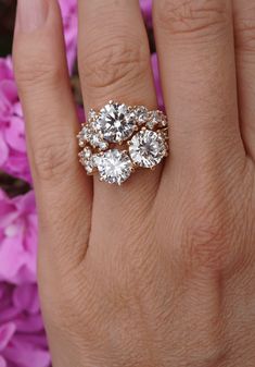 a woman's hand with three diamond rings on it and pink flowers in the background