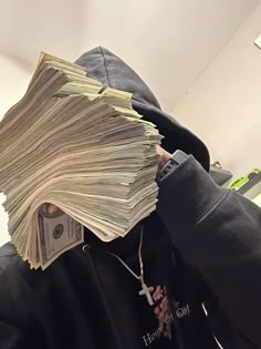 a person wearing a black hoodie with stacks of money covering their face