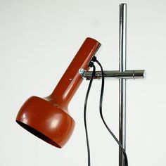 an orange table lamp on a white wall next to a metal pole with a black cord