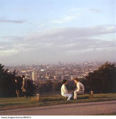 two men sitting on a bench in front of the city