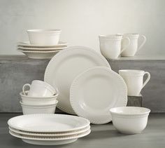 white dishes and cups are stacked on top of each other in front of a gray wall