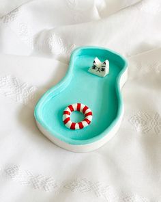 a blue bowl with candy canes in it on a white bed sheet next to an eyeglass holder