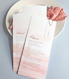 two pink and white wedding programs on a plate