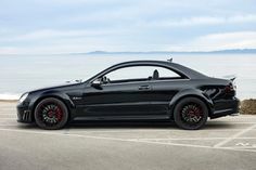 a black car parked in a parking lot next to the ocean