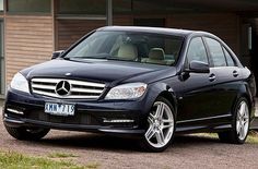 a black mercedes c class parked in front of a brown brick building with grass and bushes