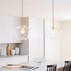 two lights hanging from the ceiling above a table in a room with white walls and cabinets