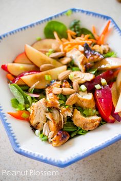 a salad with chicken, apples and carrots in a blue and white bowl