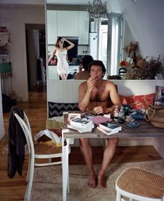 a shirtless man sitting at a table in front of a mirror with books on it