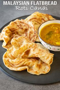 malaysian flatbread roti canai served with soup and pita bread on a black plate