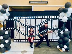 two people are playing guitar in front of a backdrop with balloons and black and white decorations