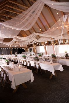 a banquet hall with tables covered in white cloths and lights hanging from the ceiling