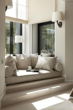 a window seat in the corner of a living room with pillows and blankets on it