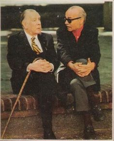 two men in suits sitting on a stone bench talking to each other with canes