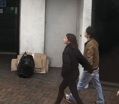 two women walking down the sidewalk in front of a building with boxes and bags on it