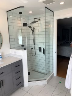 a bathroom with a walk in shower next to a white sink and gray cabinetry