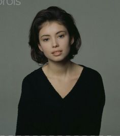 a woman with short hair wearing a black sweater and posing for a photo in front of a gray background