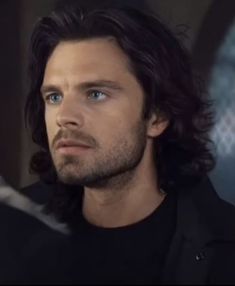 a man with long hair and blue eyes looks at something in the distance while wearing a black shirt