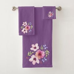 two purple towels with flowers on them hanging from a towel rack in front of a white wall