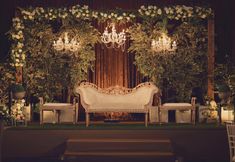 an elegant wedding set up with chandeliers and greenery on the wall behind it