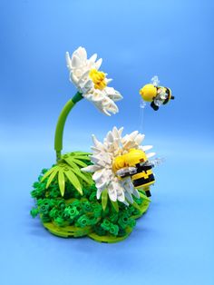 two bees are flying over some flowers on a blue surface with green grass and white daisies