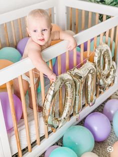 a baby sitting in a crib next to balloons