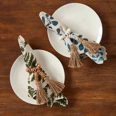 two white plates topped with tassels on top of a wooden table