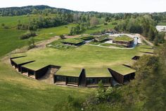 an aerial view of a large green field with several buildings on it and trees in the background