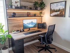 a desk with a computer on top of it in front of some pictures and plants