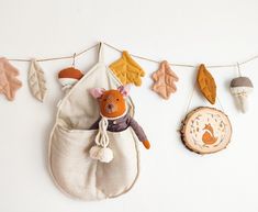 a stuffed animal hanging from a clothes line with autumn leaves on the wall behind it