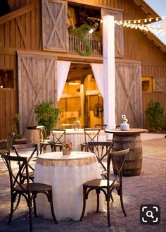 an outdoor table and chairs in front of a barn with lights strung from the roof