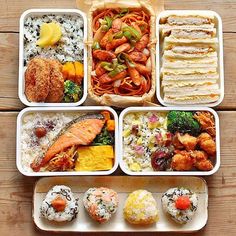 an assortment of sushi and other food items in trays on a wooden table