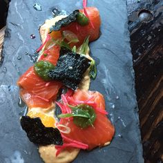 some kind of appetizer with salmon and greens on it sitting on a slate platter