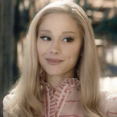 a woman with long blonde hair wearing a pink shirt and looking at the camera while smiling