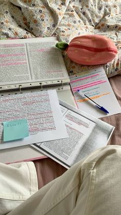 an open book sitting on top of a bed next to some papers and pencils