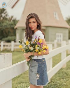 a woman holding flowers standing next to a white fence with a windmill in the background