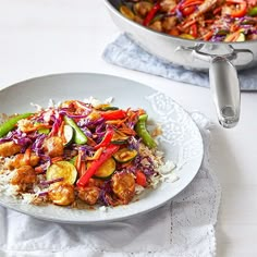 a white plate topped with chicken and veggies next to a skillet filled with rice